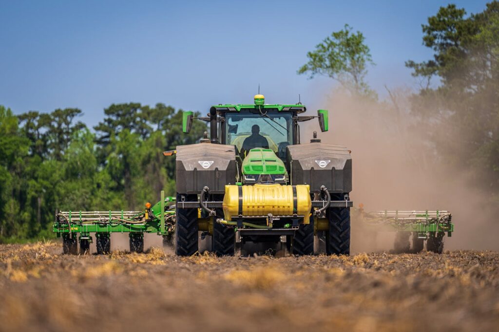 A green tractor in use for sowing on a sunny rural farm field in summer.