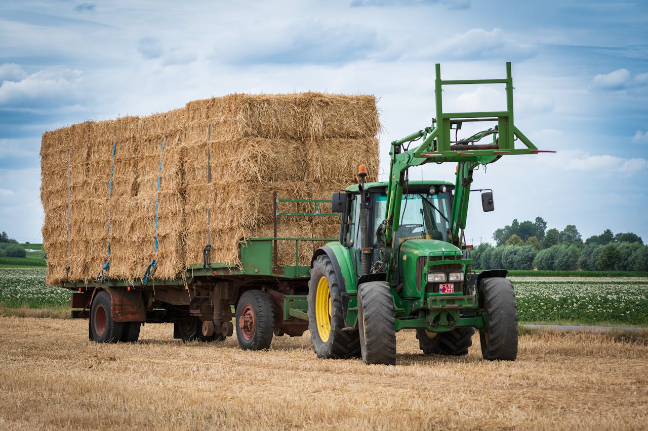 A powerful tractor hauls a full load of hay bales across a rural field under a cloudy sky.