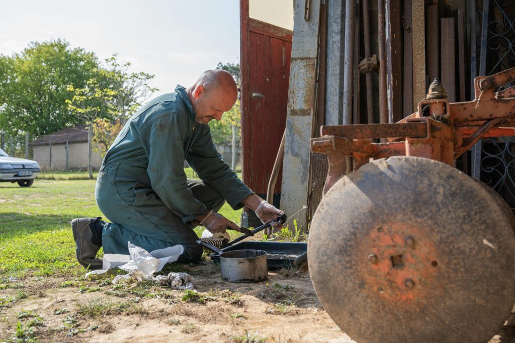 A mechanic working on farm equipment in Parcoul-Chenaud, France, under the sun.